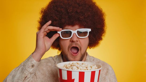 Excited bearded man with afro hairstyle eating popcorn and watching interesting tv serial, sport game, online social media movie film content. Hipster guy in 3D glasses enjoying domestic entertainment