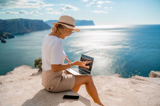 Freelance women sea working on the computer. Good looking middle aged woman typing on a laptop keyboard outdoors with a beautiful sea view. The concept of remote work