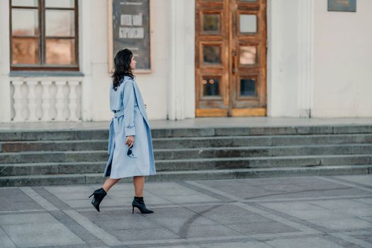 Woman walks in the city, lifestyle. Young beautiful woman in a loose light sweater, brown skirt and sneakers with a hat