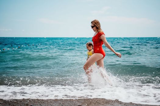 Happy loving family mother and daughter having fun together on the beach. Mum playing with her kid in holiday vacation next to the ocean - Family lifestyle and love concept.