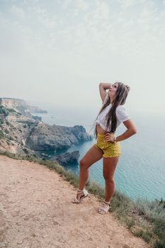 Woman travel sea. Happy tourist taking picture outdoors for memories. Woman traveler looks at the edge of the cliff on the sea bay of mountains, sharing travel adventure journey.