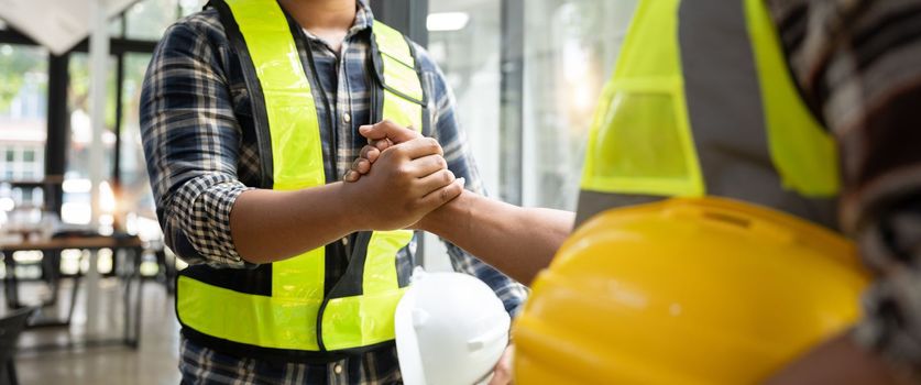 Construction engineer and architect with blueprint shaking hands while standing on construction site. Home building concept.