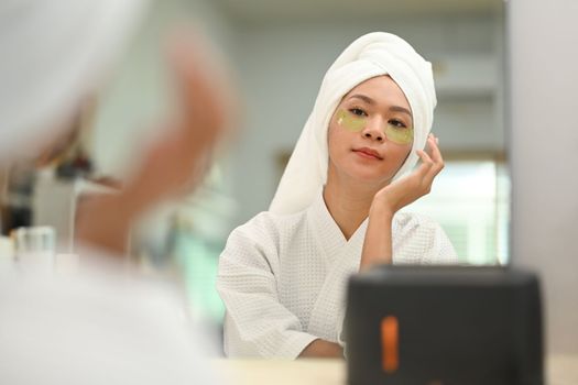 Charming millennial woman in bathrobe applying patches under eyes. Beauty treatment, skincare and cosmetics concept.