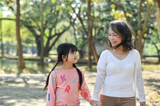 Adorable little child and elderly grandmother walking in the park, spending time outdoor together. Family and love concept.