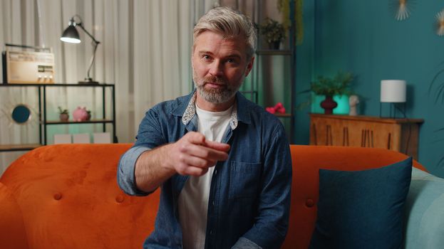 Hey you. Middle-aged old man smiling excitedly and pointing to camera, choosing lucky winner, indicating to awesome you, inviting, approve. Mature senior gray-haired guy at home night room apartment