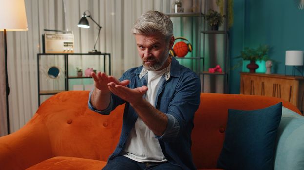 Bearded cheerful rich senior mature man showing wasting, throwing money around hand gesture, more tips earnings, big profit, win lottery, body language, share. Middle-aged guy at home in evening room
