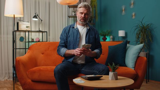 Planning budget. Rich middle-aged man counting money cash use calculator and calculate domestic bills at home. Mature old guy satisfied of income earnings, win, saves money for planned vacation, gifts