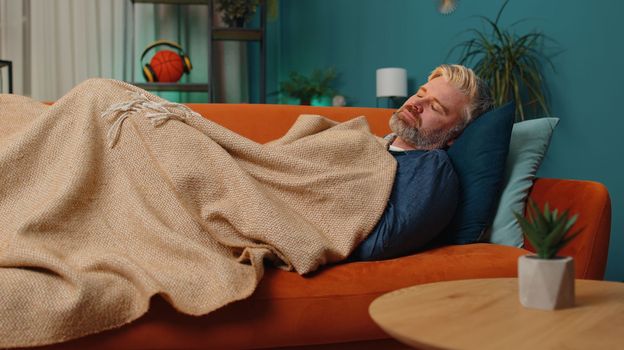 Tired middle-aged man lying down in bed taking a rest at home. Carefree mature senior gray-haired guy napping, falling asleep on comfortable sofa with pillows. Closed his eyes enjoy night nap alone