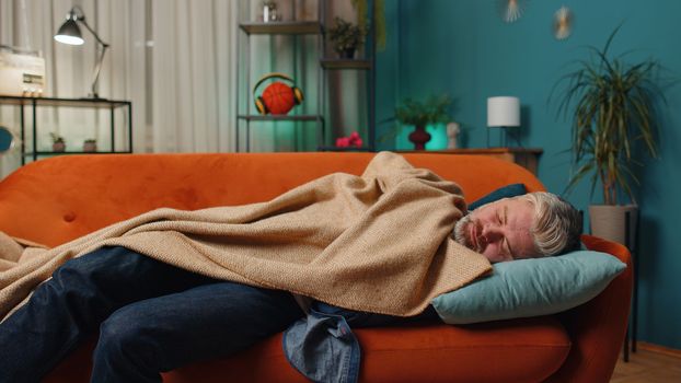 Tired middle-aged man lying down in bed taking a rest at home. Carefree mature senior gray-haired guy napping, falling asleep on comfortable sofa with pillows. Closed his eyes enjoy night nap alone