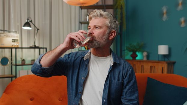 Thirsty middle-aged man holding glass of natural aqua make sips drinking still water preventing dehydration at home. Mature senior old guy with good life habits, healthy slimming, weight loss concept