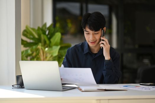 Handsome male financial advisor looking at document and talking on mobile phone with client.