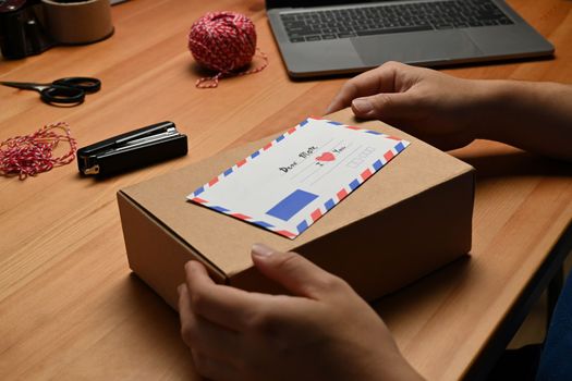 Close up view of man hands holding gift box with greeting card, preparing present for family during holiday season.