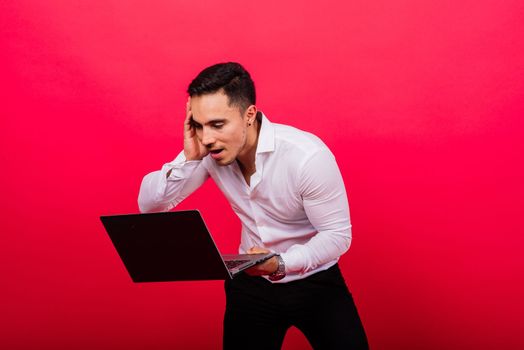 Image of young cheerful businessman holding and using laptop isolated over red background