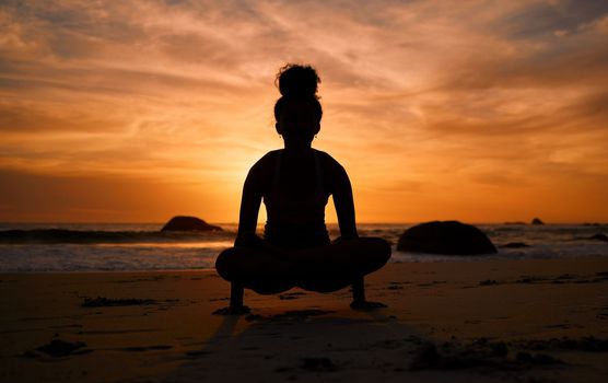 Sunset, yoga and silhouette of a woman on the beach in a lotus pose doing a meditation exercise by the sea. Peace, zen and shadow of a calm female doing a pilates workout outdoor at dusk by the ocean.