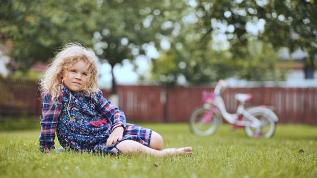A little girl in the garden on the grass with her bicycle in the background
