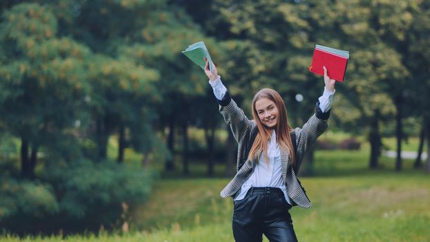 A cheerful student with books in the park in the summer
