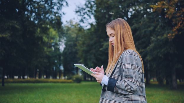 A young girl walks with a tablet in the park