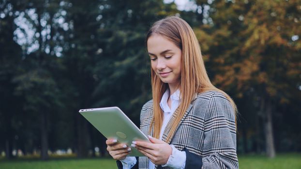 A young girl walks with a tablet in the park