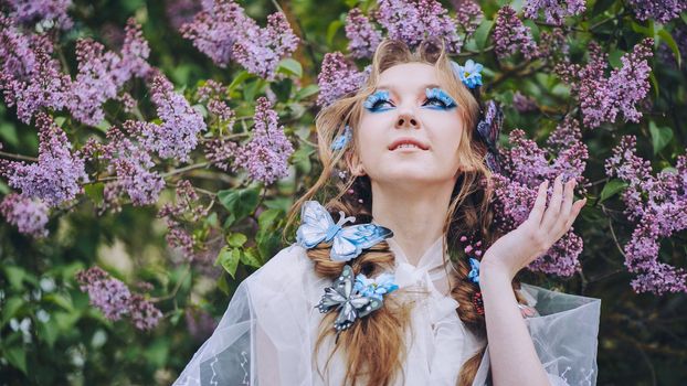 A young girl poses in lilac with a beautiful hairstyle of flowers and butterflies