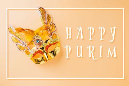Happy Purim carnival decoration. Golden venetian ball mask isolated on pastel background with copy space, Jewish Purim or Mardi Gras in Hebrew, celebration holiday background banner design
