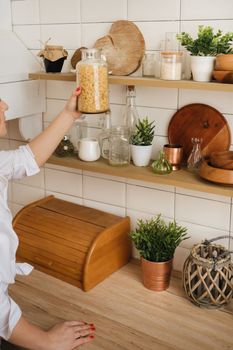 Close-up of the hostess's hands taking a jar of pasta on a shelf in the kitchen.