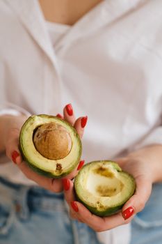 Close-up of a girl's hand holding an avocado cut in two.