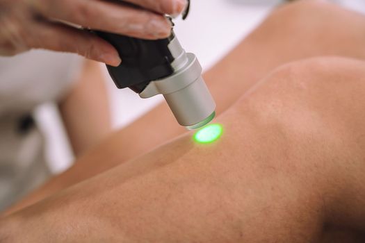 Close up shot of gloved hand with the laser hair removal machine's handpiece along woman leg. Alexandrite laser techhnology removing hair. Beauty procedureBeauty technology concept