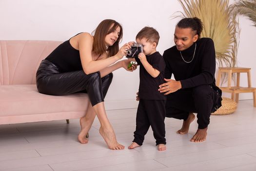 Stylish multiracial happy young family in black clothes, in the light living room, playing with an old camera