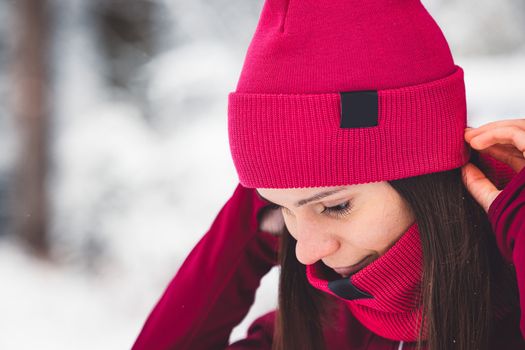 Beautiful young caucasian woman with brown hair, wearing a red jacket and a hat outside in the forest when it's snowing. Woman walking around a snowy forest. Woman holding a to go cup with tea.