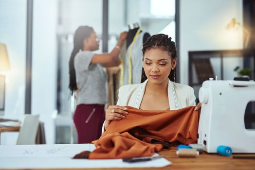 Fashion is about fabric. a young fashion designer sewing garments while a colleague works on a mannequin in the background