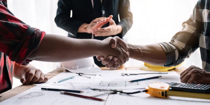 Shaking hands, Blueprints architects and building engineers talking meeting and planning will chronicle the design and technical aspects of a new house construction, renovation remodeling