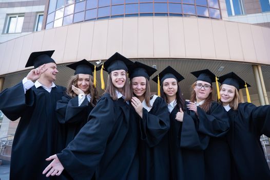 Happy students in graduate gown stand in a row against the backdrop of the university