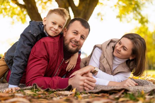 cheerful traditional family with little son lies on autumn leaves in the park with smiles.