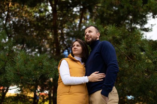 happy adult husband and wife in the autumn forest stand embracing and look into the distance.