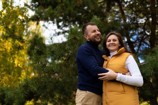 a happy husband joyfully hugs his wife against the backdrop of an autumn forest.