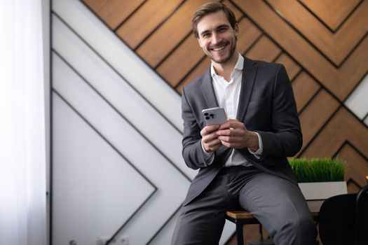 successful male businessman in a business suit with a smile on his face with a phone in his hands sits leaning on the table.