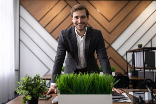 the manager in the office greets the new employee standing up from the table with a smile looking at the camera.