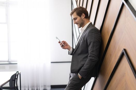 an office worker stands leaning against a wall and looks at a mobile phone.