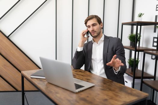 young businessman sitting at a laptop in the office talking on a mobile phone.