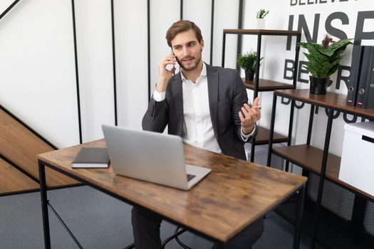 real estate agent talking on a mobile phone with a client in the office sitting in front of a laptop.