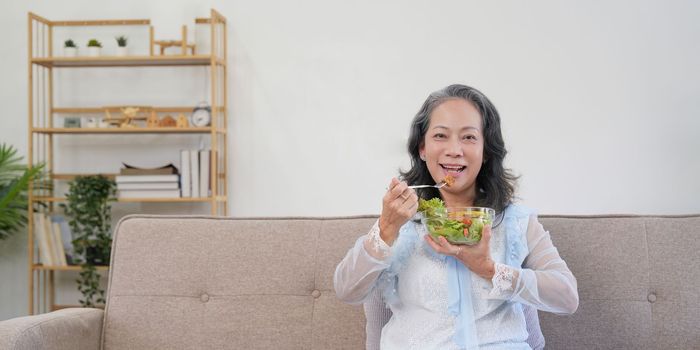 Happy old woman eating healthy vegetable salad at home.