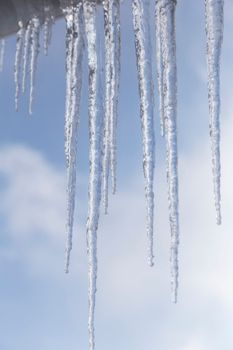 Long icicles of ice hang from the roof of the house. Presented against a background of blue sky with clouds