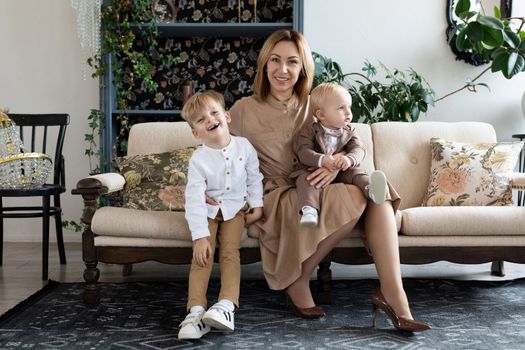 mother with two small children in a cozy atmosphere sit on the sofa and look at the camera.