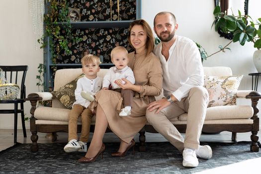 Happy family of mom dad and 2 little sons sitting on the sofa In beige clothes.