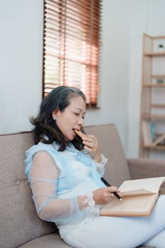 Portrait of an elderly Asian woman holding a notebook eating snacks and drinking tea