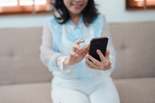 Portrait of an elderly Asian woman holding a mobile phone with eating snacks and drinking tea