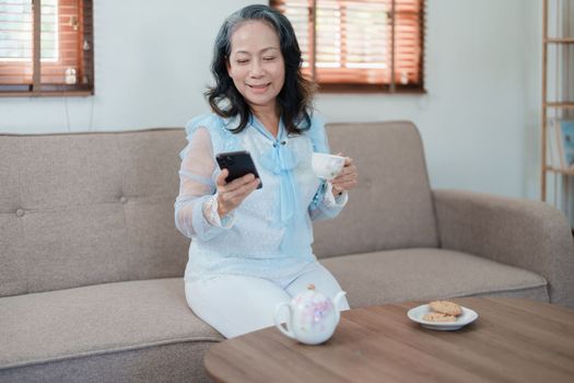 Portrait of an elderly Asian woman holding a mobile phone with eating snacks and drinking tea