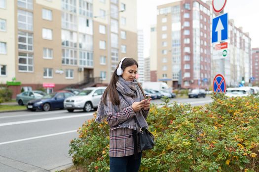 stylish young woman on a crosswalk in headphones looks at a mobile phone.
