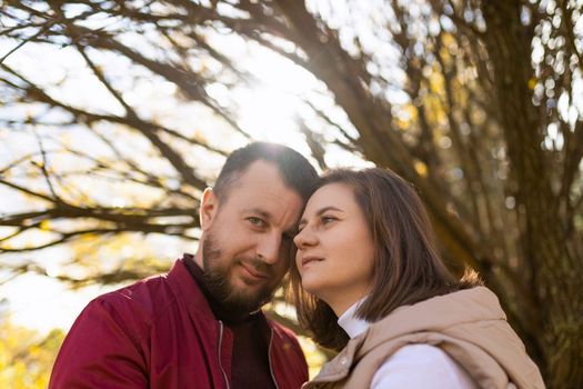 an adult married couple stand to each other against the background of a branchy autumn tree, close-up portrait.