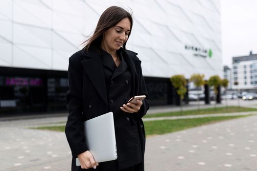 woman Businessman with a laptop in his hands looks at a mobile phone on the background of an office building.